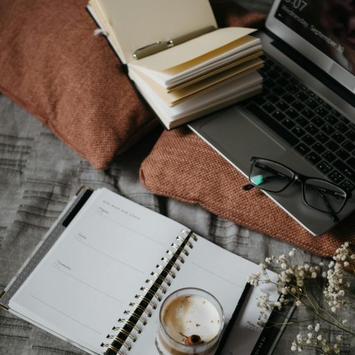 A warm, inviting home workspace featuring a notebook, laptop, and coffee on a soft surface.